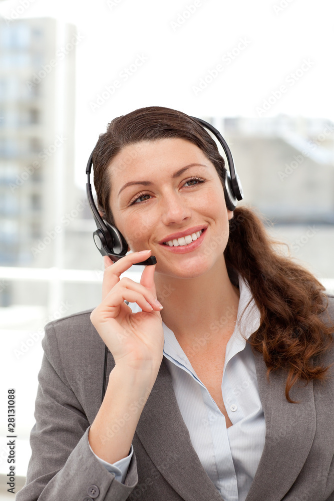 Cheerful businesswoman using earpiece sitting at her desk Cheerful businesswoman using earpiece sitting at her desk