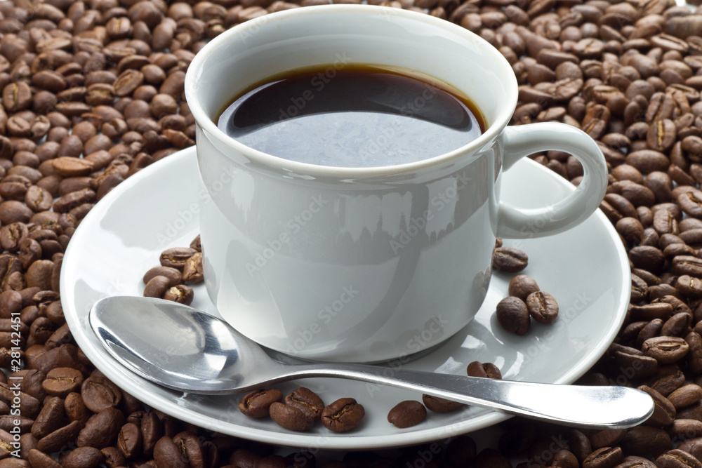 Coffee beans in white cup on saucer with spoon Coffee beans in white cup on saucer with spoon