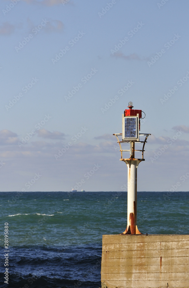 Little solar lighthouse on a concrete jetty with sea and sky
