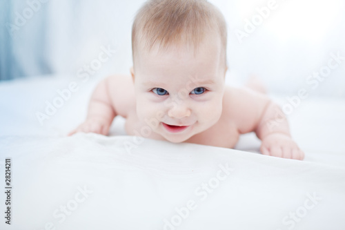 Happy smiling infant baby girl on white sheet photo