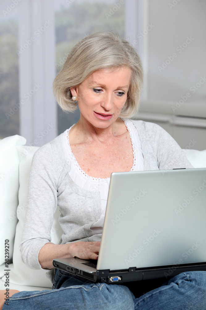 Senior woman sitting in sofa with laptop computer Senior woman sitting in sofa with laptop computer