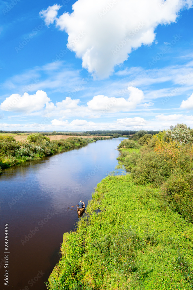 Blue river, cloud sky, green shores and small boat.