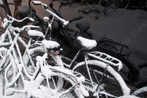 snow-covered bikes with reflections in black shopping window