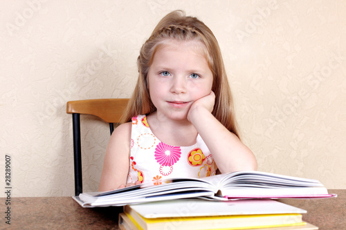 Little girl reading book in the kitchen against yellow wall at h