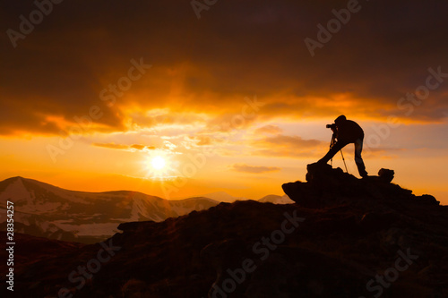silhouette of a photographer who shoots a sunset in the mountain