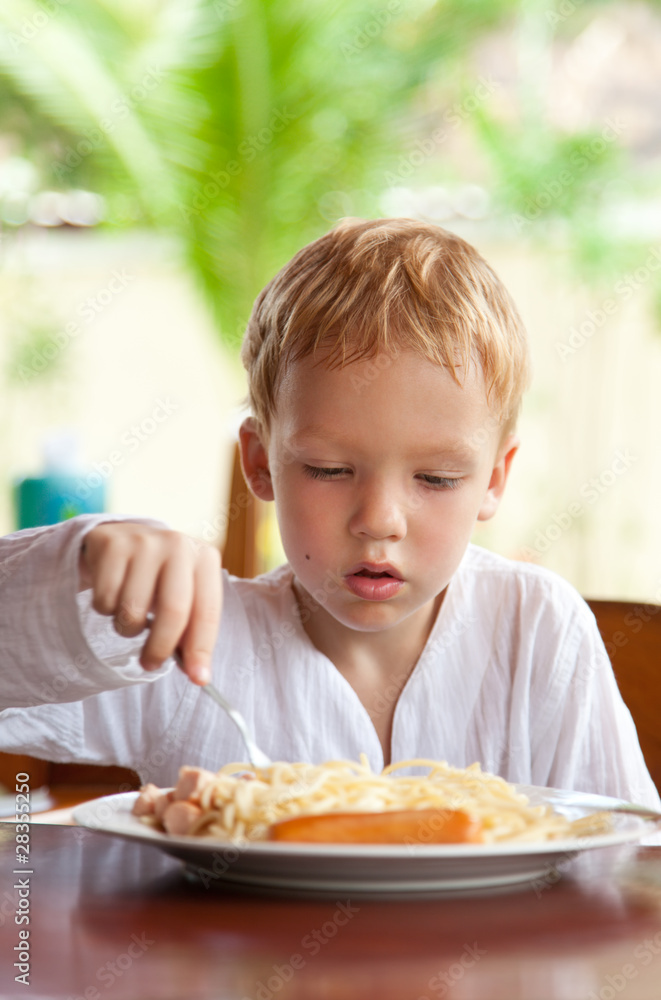 Four year old boy eating spaghetti with sausages outdoors Four year old boy eating spaghetti with sausages outdoors