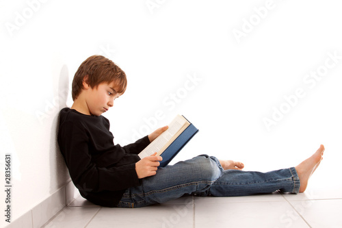 Quadro su tela Junge liest am Boden sitzend, konzentriert ein Buch