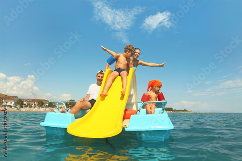 family with boy and girl on pedal boat with yellow slide in sea photo