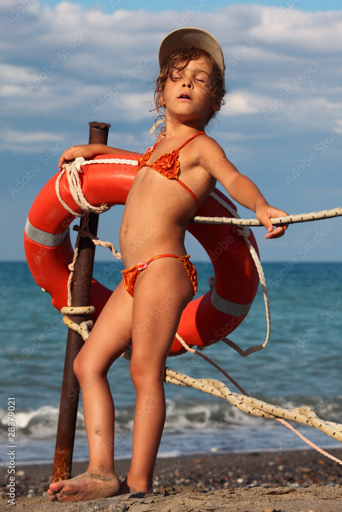 beautiful little girl in bathing suit and cap standing on beach