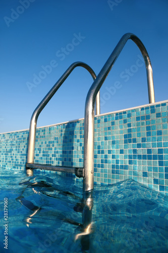 shiny chrome ladder into pool, blue sky, blue water, blue bottom