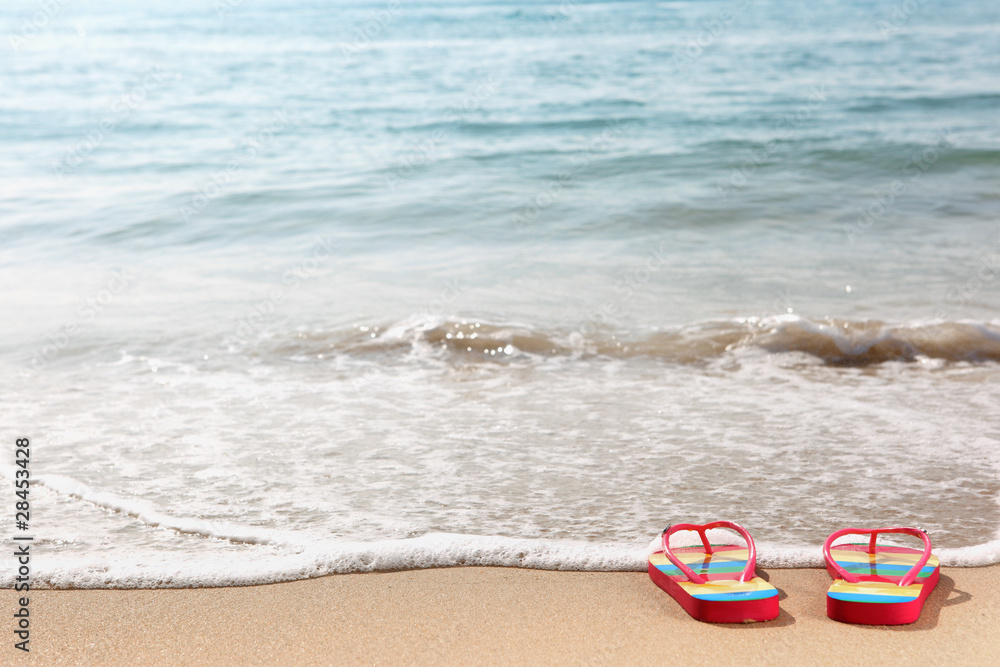 Naklejka premium Flipflops on a sandy ocean beach