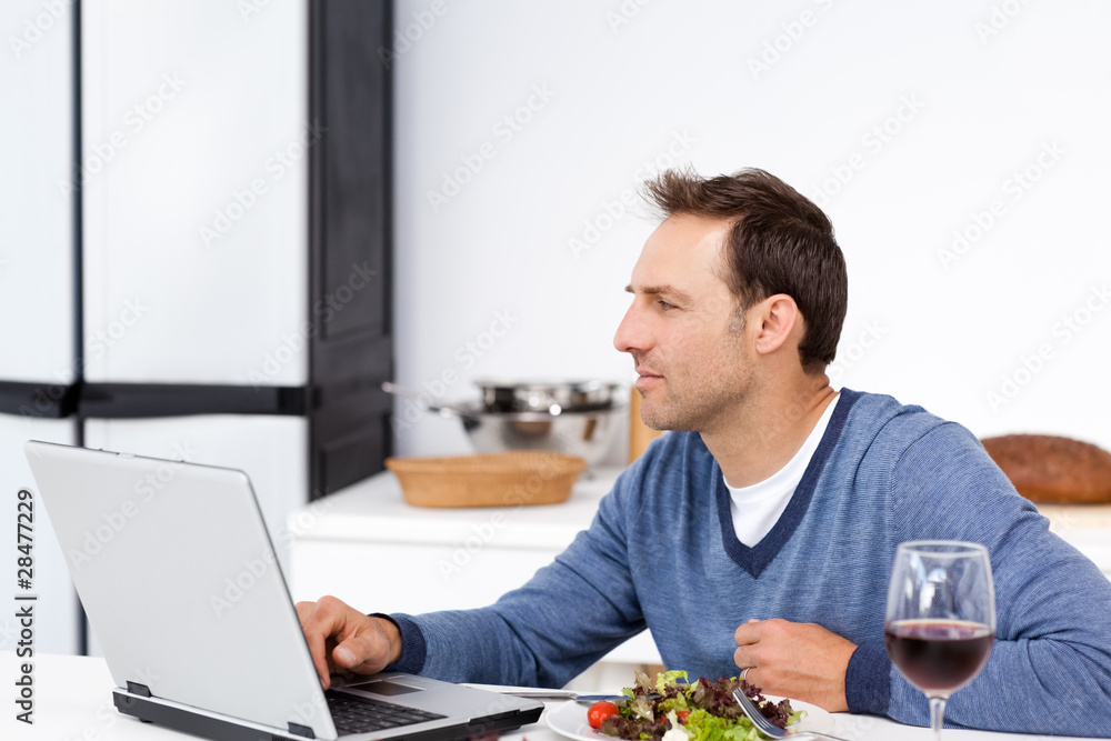 Concentrated man looking at his laptop while eating a salad Concentrated man looking at his laptop while eating a salad
