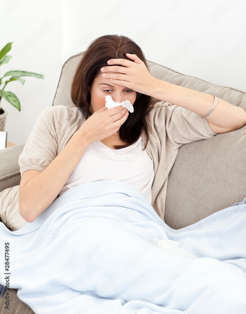 Tired woman feeling her temperature while blowing her nose Tired woman feeling her temperature while blowing her nose