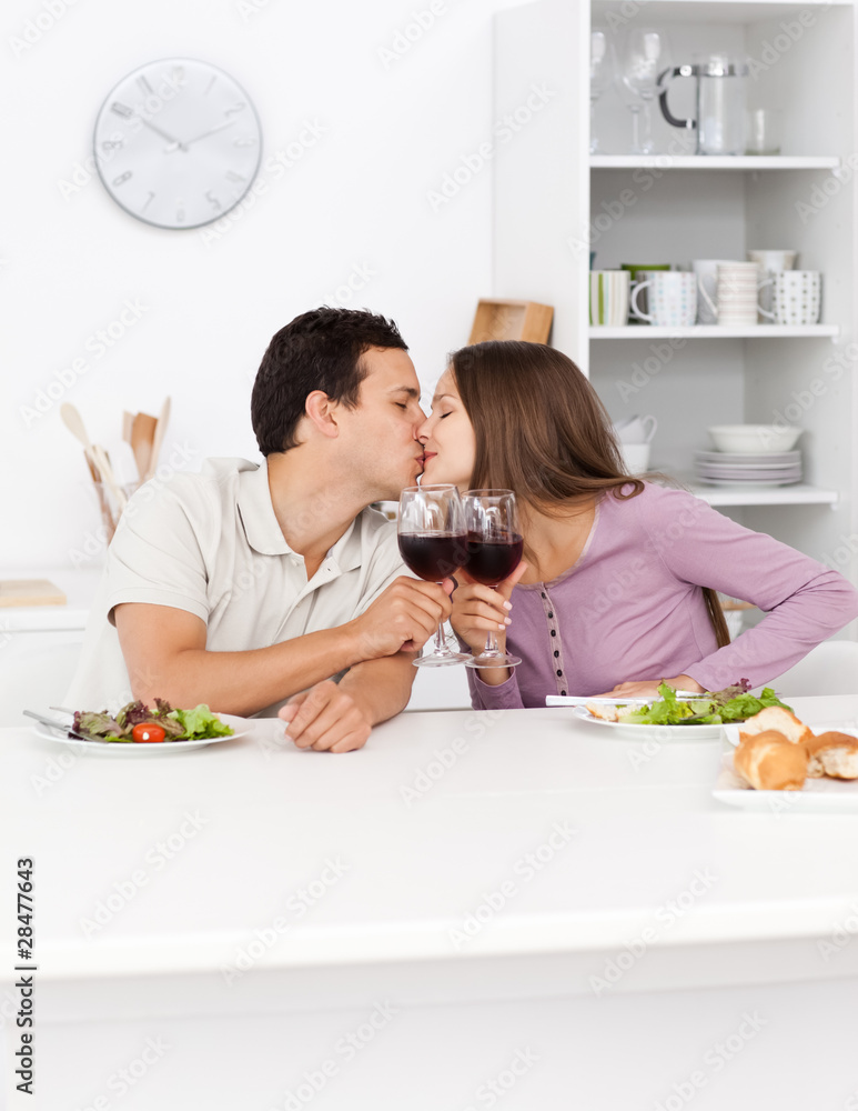 Young couple kissing with red wine in their hands during lunch