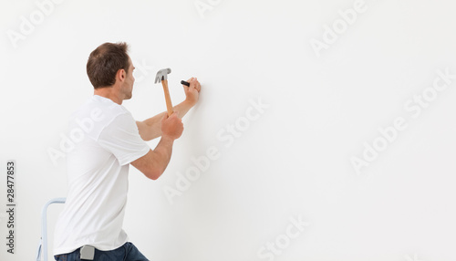 Obraz na plátně Rear view of a man hammering against a white wall