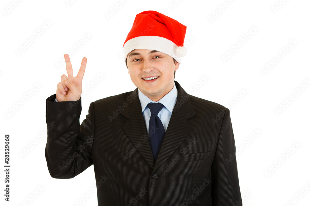 Happy young businessman in Santa hat showing victory gesture Happy young businessman in Santa hat showing victory gesture
