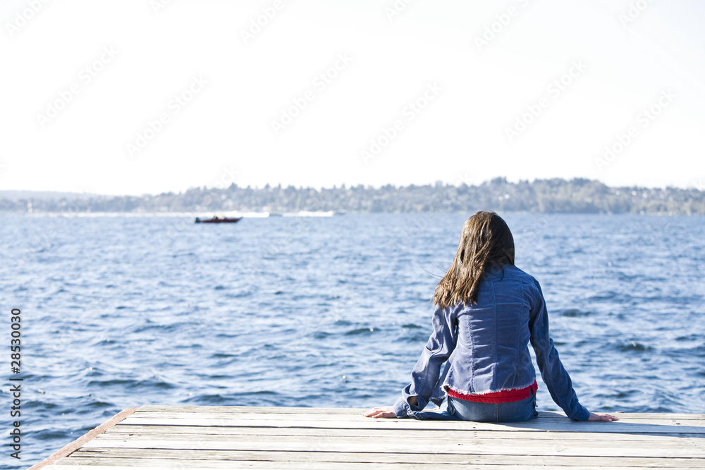 Girl sitting alone on dock by lake, looking out over water. Girl sitting alone on dock by lake, looking out over water.