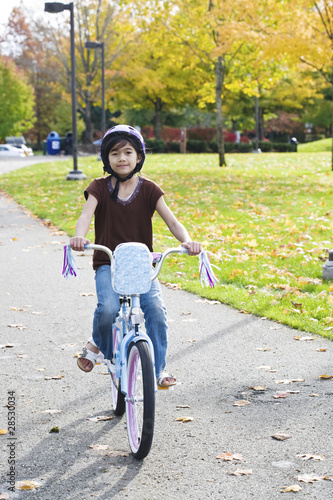 Fototapeta Naklejka Na Ścianę i Meble -  Little girl riding bike in park in late summer, early autumn