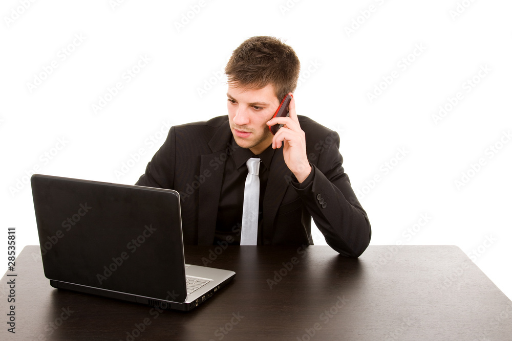 Young business man working on a desk with a laptop and talking w Young business man working on a desk with a laptop and talking w