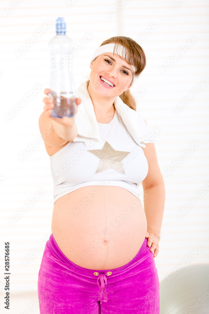 Smiling pregnant female in sportswear holding bottle of water. Smiling pregnant female in sportswear holding bottle of water.