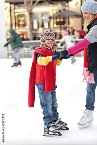 A boy hangs on to his mother while learning to ice skate.
