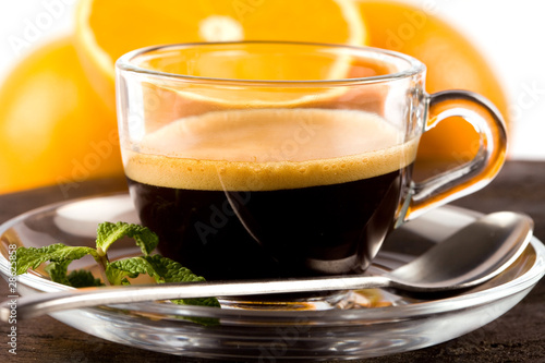 Caffè in tazza di vetro con foglie di menta e sfondo di arance