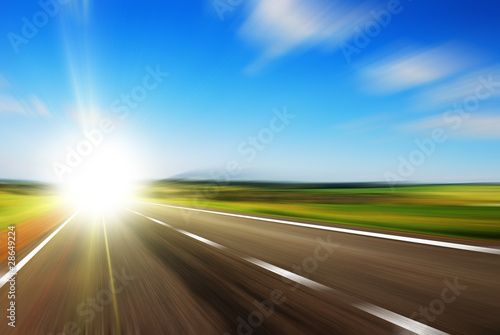 Blurred road and blue blurred sky with a shining sun © grthirteen