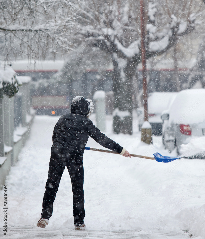 Fototapeta premium Woman shoveling snow from a sidewalk after a heavy snowfall in a
