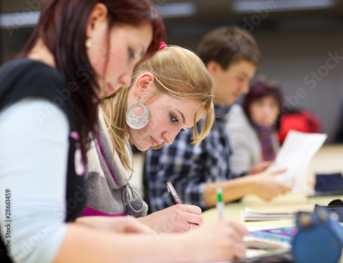 pretty female college student sitting in a classroom full of stu