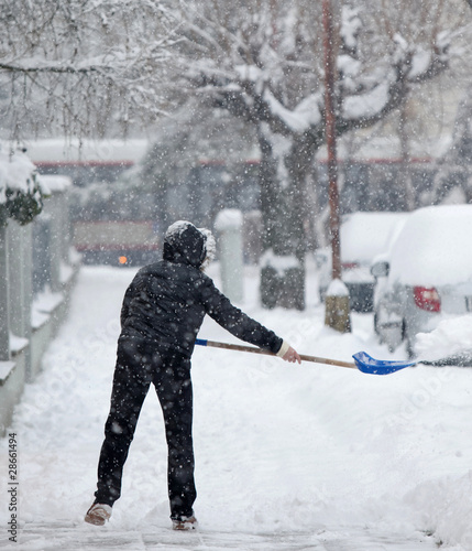 Photography Woman shoveling snow from a sidewalk after a heavy snowfall in a