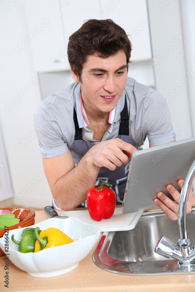 Man in kitchen looking at recipe on electronic tab Man in kitchen looking at recipe on electronic tab