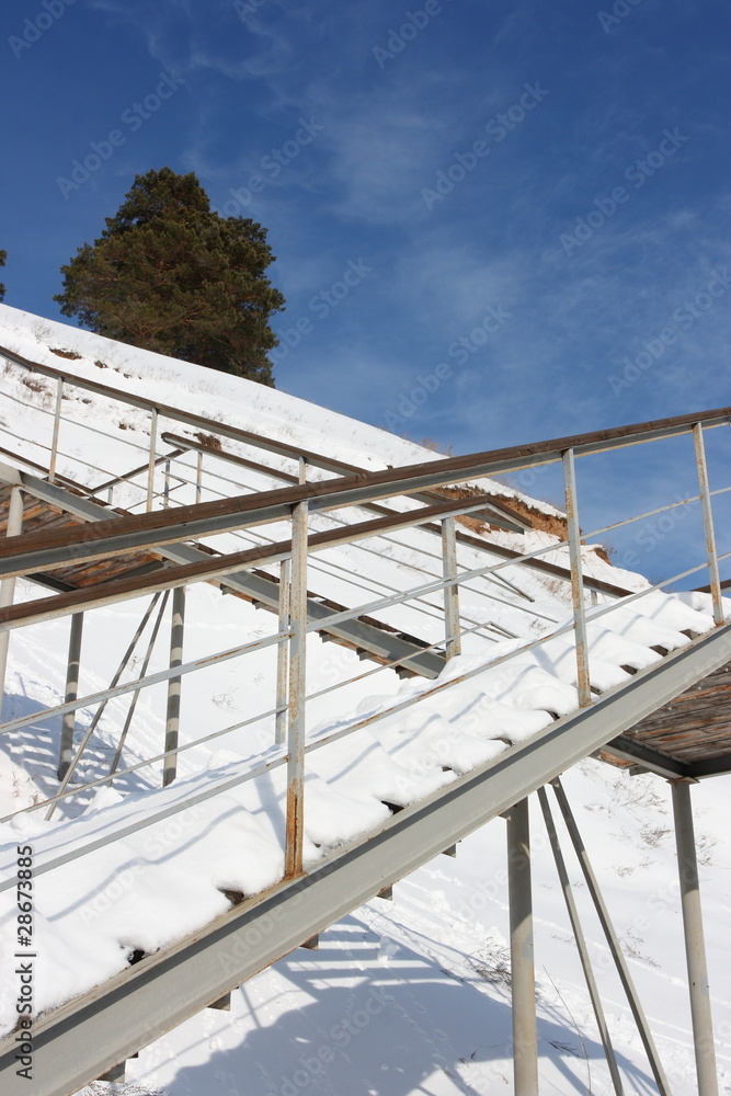 Stairs with landing against a snow slope against pines Stairs with landing against a snow slope against pines