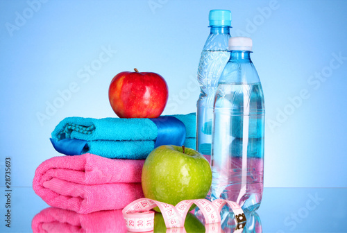 Blue bottle of water, apple, sports towel and measure tape on bl