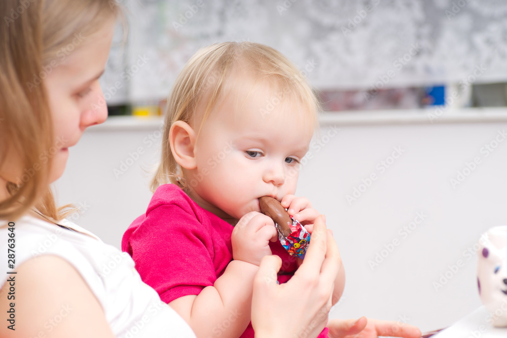 Young adorable baby eat chocolate with mother in kitchen Young adorable baby eat chocolate with mother in kitchen