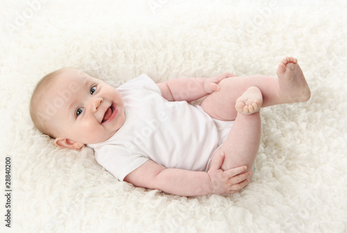 Baby lying on back smiling with feet in the air