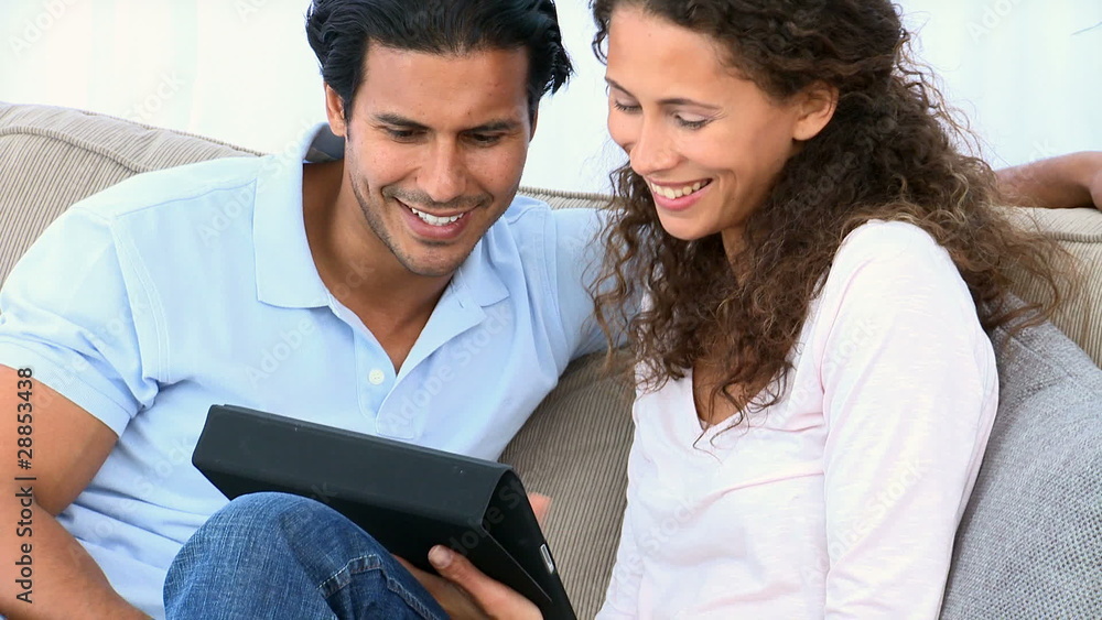Couple using a computer tablet sitting on the sofa Couple using a computer tablet sitting on the sofa