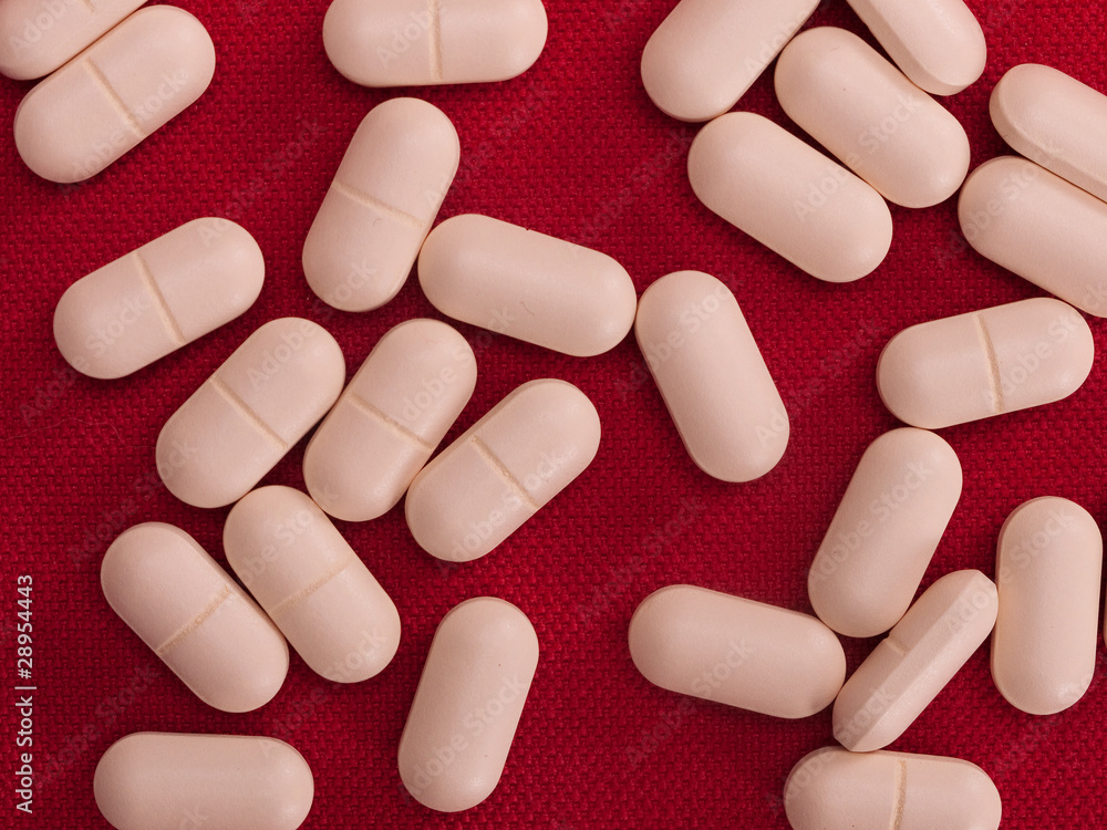 Many beige pills on red cloth Many beige pills on red cloth
