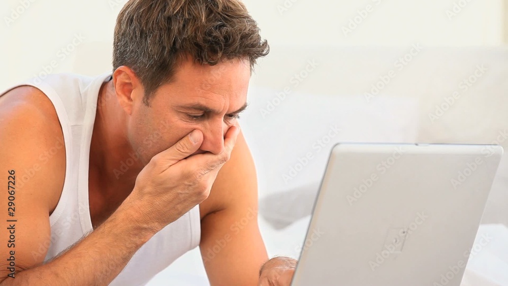Worried man searching something on his laptop on his bed Worried man searching something on his laptop on his bed