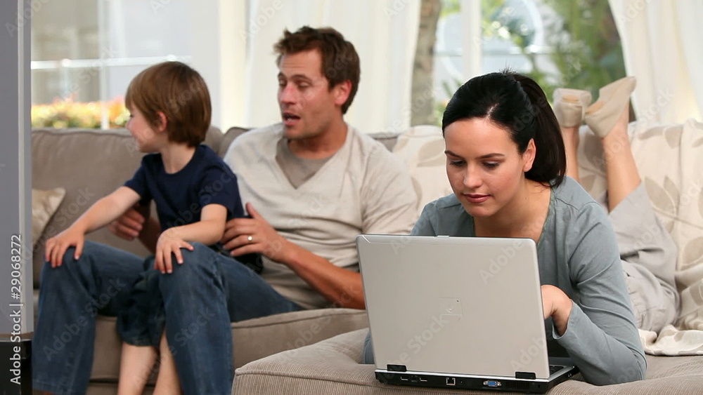 Woman using laptop with his family in the background Woman using laptop with his family in the background