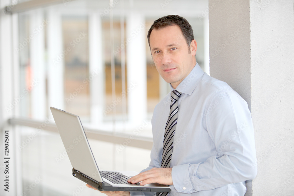 Businessman standing in hall with laptop computer Businessman standing in hall with laptop computer