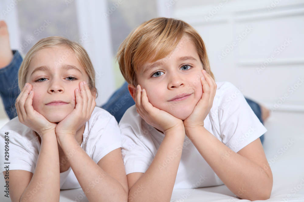 Blond children laying in sofa with hands on chin Blond children laying in sofa with hands on chin