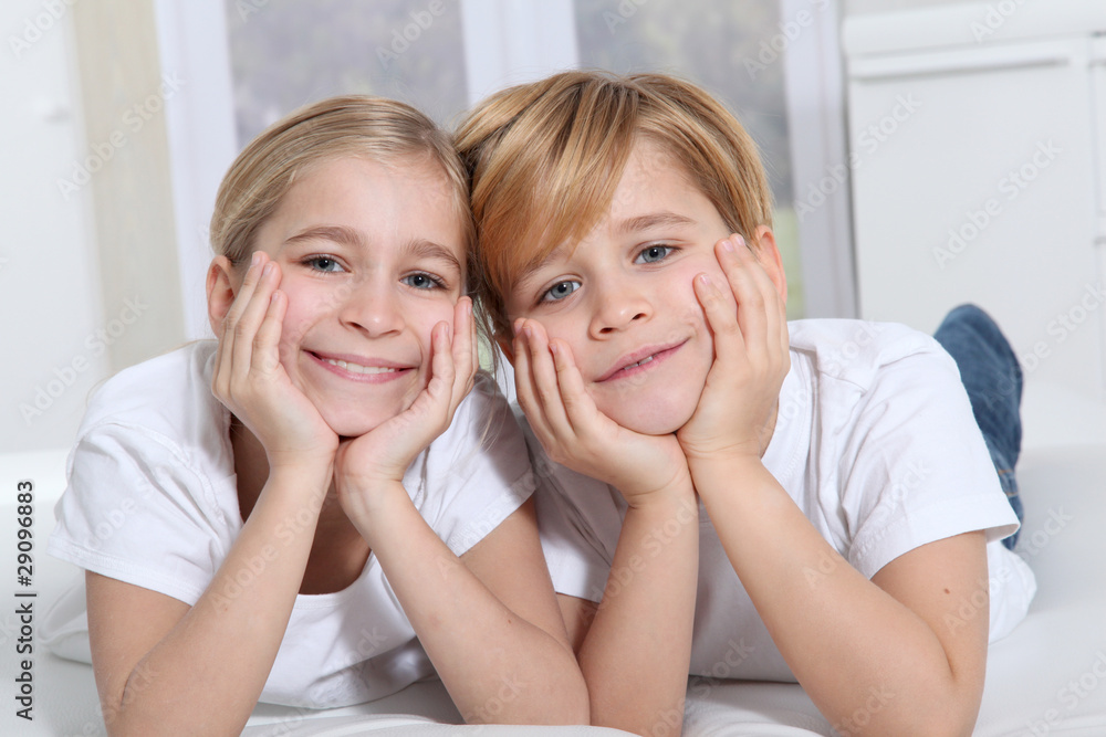 Blond children laying in sofa with hands on chin Blond children laying in sofa with hands on chin