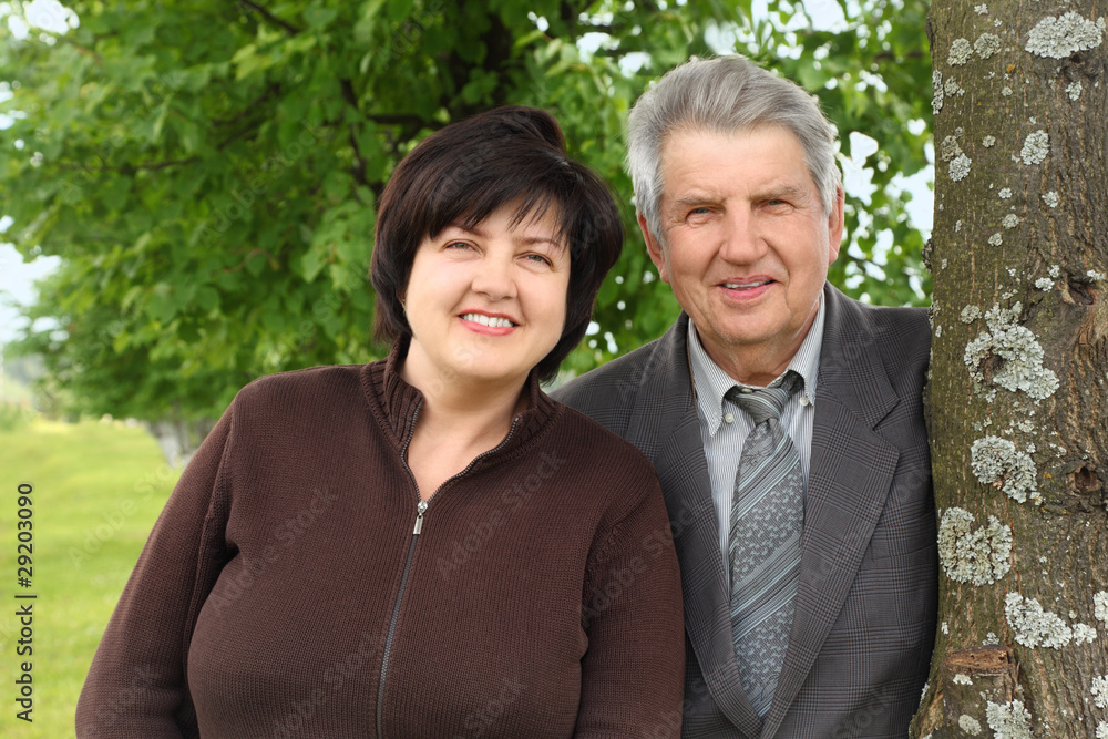 old senior and his adult daughter standing near tree and smiling old senior and his adult daughter standing near tree and smiling