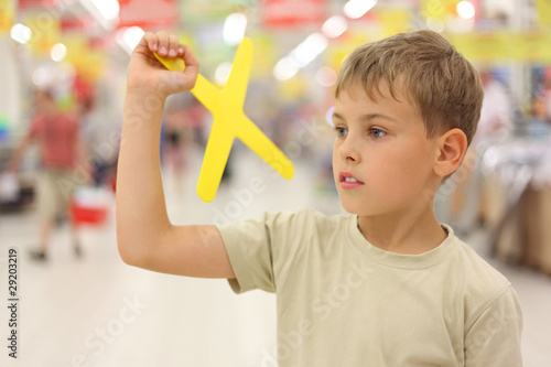 little boy holding yellow boomerang toy, standing in shop photo