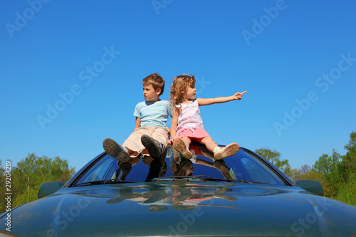 little boy and girl sitting on car roof on blue sky © Pavel Losevsky