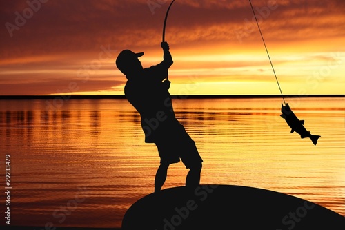 Fisherman with fishing tackle and catching fish at sunrise