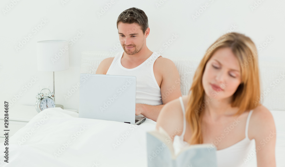 Man is on his laptop while his wife is reading a book Man is on his laptop while his wife is reading a book
