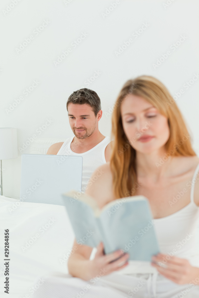 Man is on his laptop while his wife is reading a book Man is on his laptop while his wife is reading a book