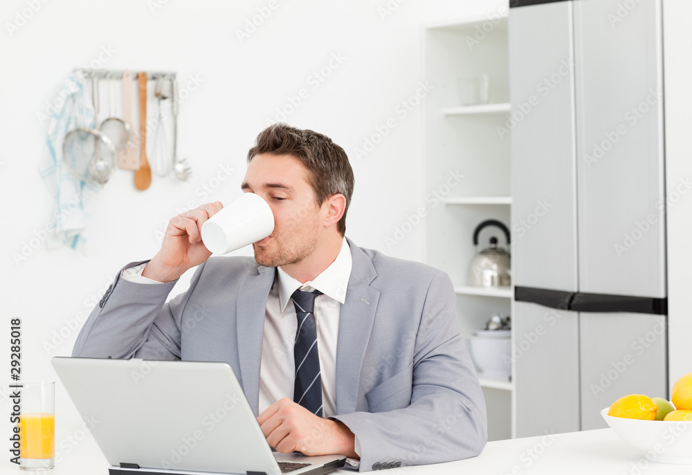 Businessman drinking while he is looking at his laptop Businessman drinking while he is looking at his laptop