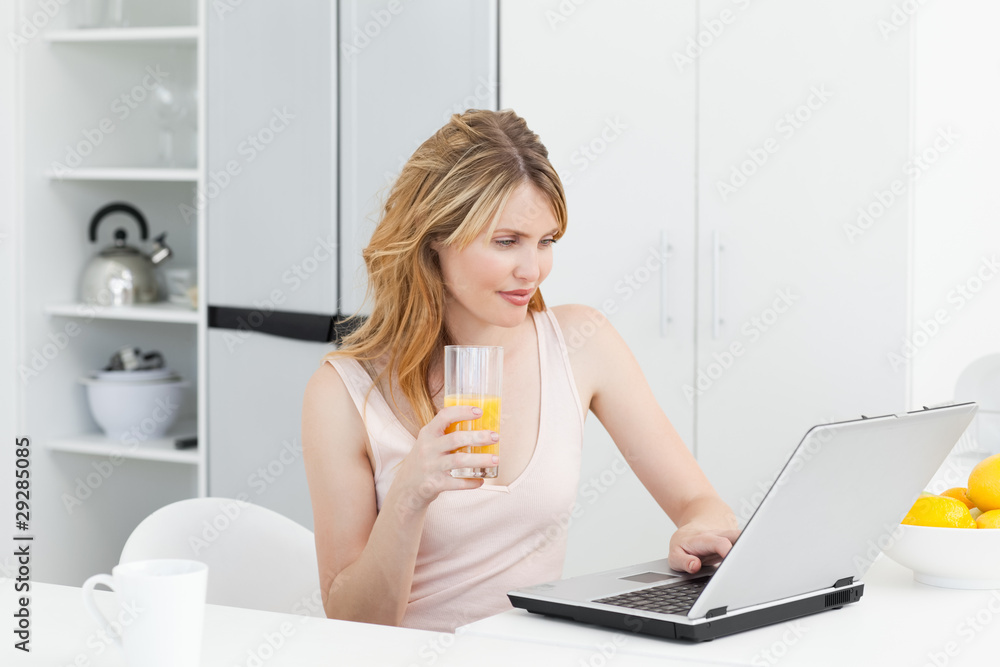 Woman drinking while she is looking at her laptop Woman drinking while she is looking at her laptop